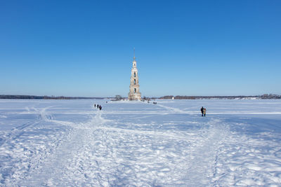 People on snow covered land against clear blue sky