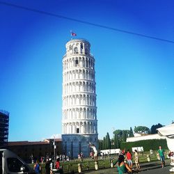 Low angle view of tourists against clear blue sky