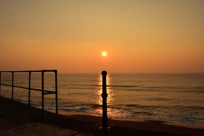 Silhouette bollard and fence by sea against clear sky during sunset