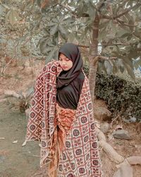 Young woman standing against tree