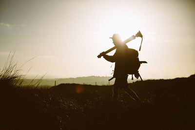 Side view of photographer walking on field against sky during sunny day