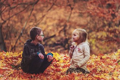 Rear view of friends sitting on land during autumn