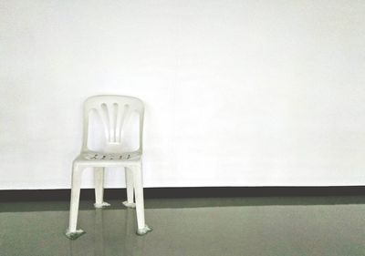 Empty chair and table against white wall