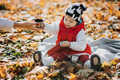 Happy little toddler baby daughter with red thermos and cup in autumn picnic in fall nature