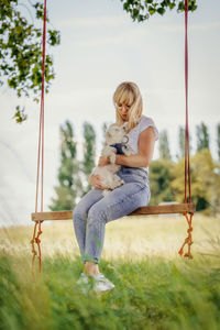 Young woman with a white dog on a tree swing.