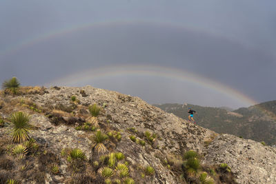 One man trail running up on a rock under a double rainbow
