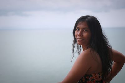 Portrait of young woman looking away against sea