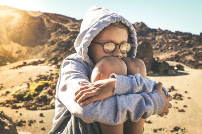 Boy hugging knees while sitting on land during sunny day