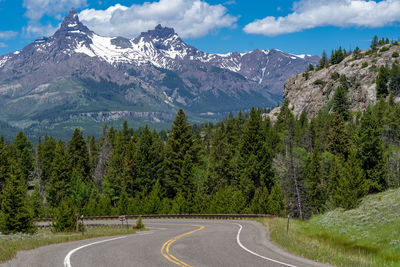 Road amidst trees and mountains against sky