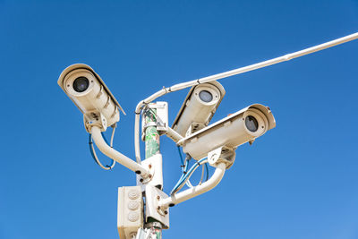 Low angle view of security cameras against clear blue sky