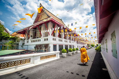 Rear view of monk walking by temple against sky