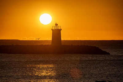 Lighthouse by sea against sky during sunset