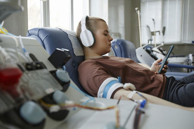 Young woman listening to music through headphones and donating blood