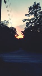 Silhouette trees by road against sky during sunset