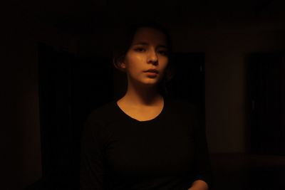 Portrait of beautiful young woman standing against black background