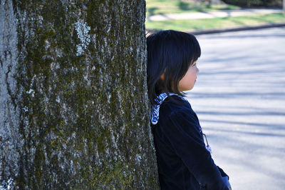 Side view of girl leaning against a tree trunk