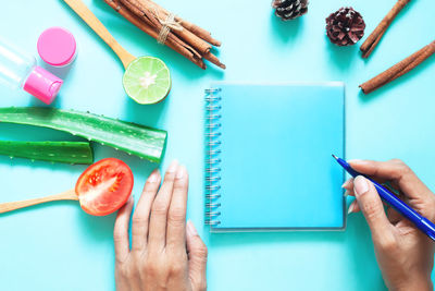 Cropped hands of woman writing in spiral notebook against blue background