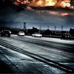 Cars on road against cloudy sky
