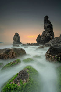 Scenic view of rocks in sea against sky during sunset