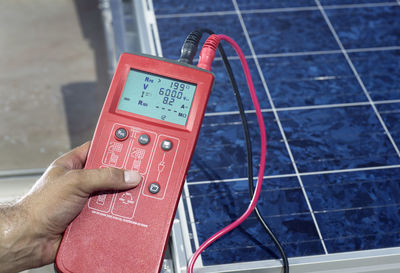 Man's hand holding measuring device in front of solar plant, close-up