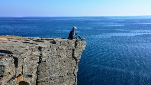 Side view of man on cliff against blue sky