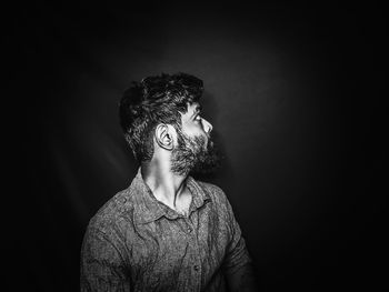 Portrait of young man looking away against black background