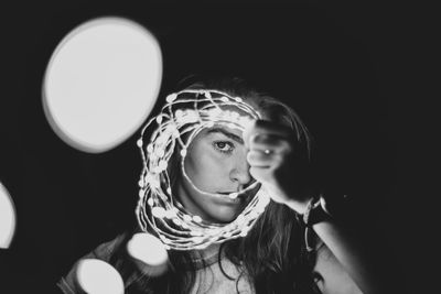 Portrait of woman holding illuminated string light against black background