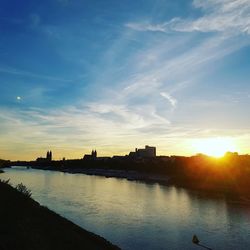 Silhouette buildings by river against sky during sunset