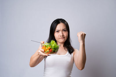 Portrait of young woman holding ice cream against white background