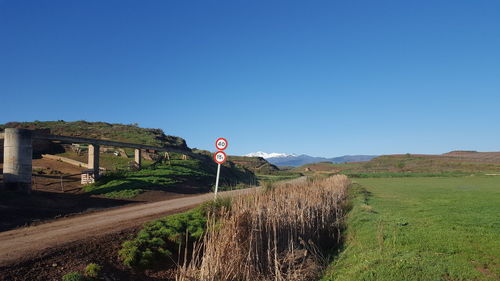 Road sign on field against clear blue sky