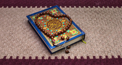 High angle view of beaded necklace with koran on carpet