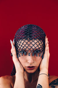 Close-up portrait of beautiful woman wearing net scarf against red background