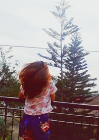 Rear view of woman standing by railing against sky