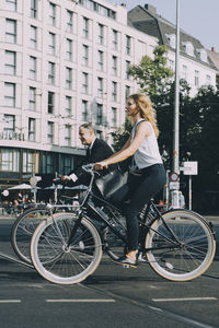 Male and female coworkers riding on street bicycle against building in city