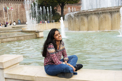 Full length of woman sitting by fountain outdoors