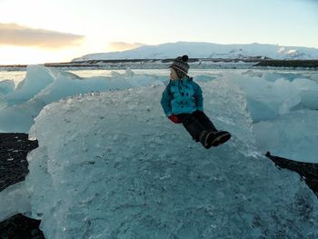 Full length of boy sitting on iceberg against sky