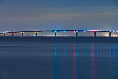 Illuminated bridge over sea against sky at night