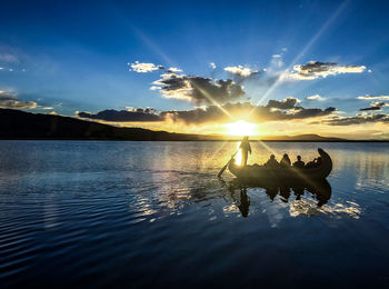 Silhouette people on lake against sky during sunset