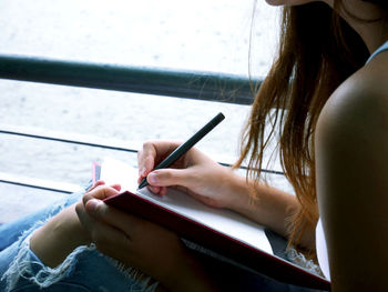 Midsection of woman writing in book while sitting against lake