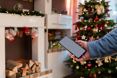 Midsection of man using mobile phone on christmas tree