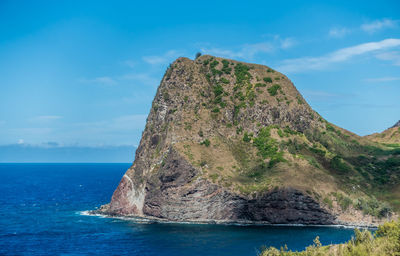 Rock formation by sea against blue sky