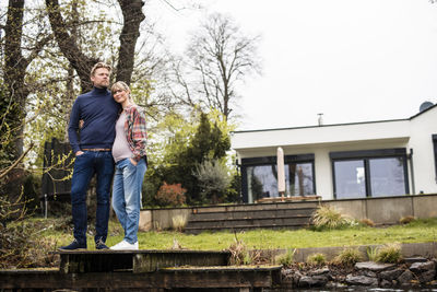 Expectant couple standing on jetty in front of house