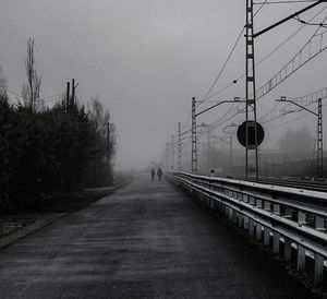 Road by electricity pylon against sky