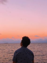 Rear view of man looking at sea against sky during sunset