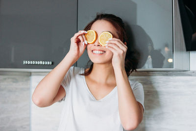 Portrait of smiling woman holding slice of lemon on face