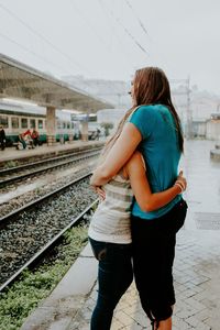 Happy young female friends embracing at railroad station during monsoon