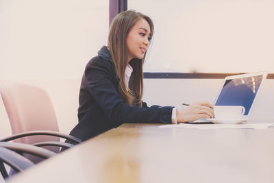 Young woman using mobile phone while sitting on table