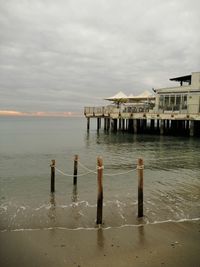 Wooden post in sea by building against sky