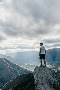 Rear view of man standing on cliff against cloudy sky
