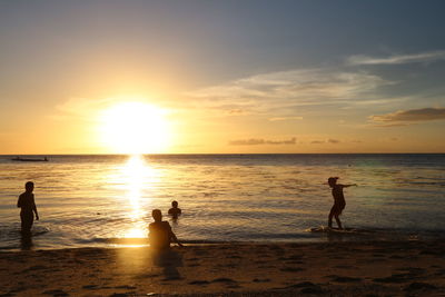 Silhouette friends enjoying at beach during sunset